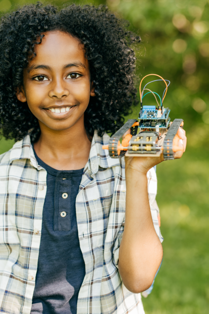 A kid smiles while holding a remote-controlled car they made.
