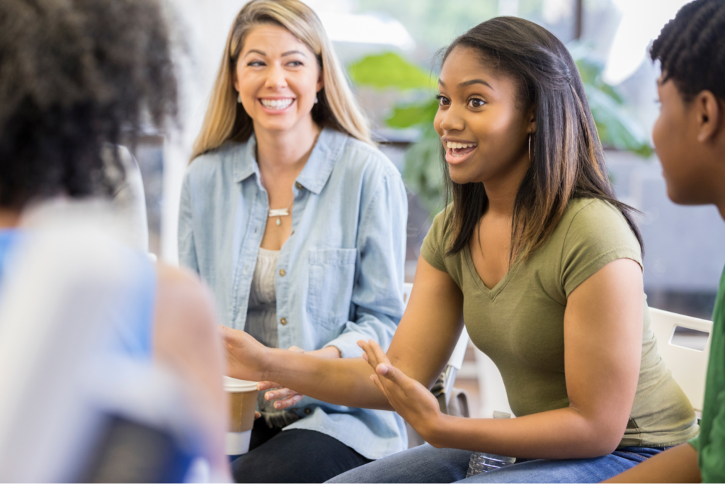 Adults and other teens listen as one student enthusiastically shares her thoughts.