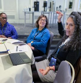 3 people sit around a circular table engaging in conversation at the NSLA conference